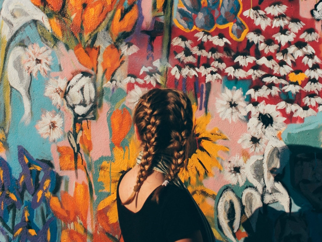 Lettipäinen tyttö seisoo värikkään seinän edessä